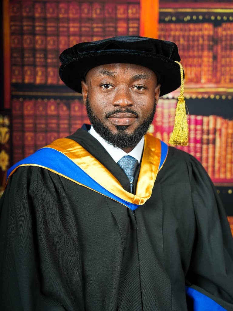 Professional portrait of Dr. Azubuike Hope Amadi in doctoral academic regalia against a library background.